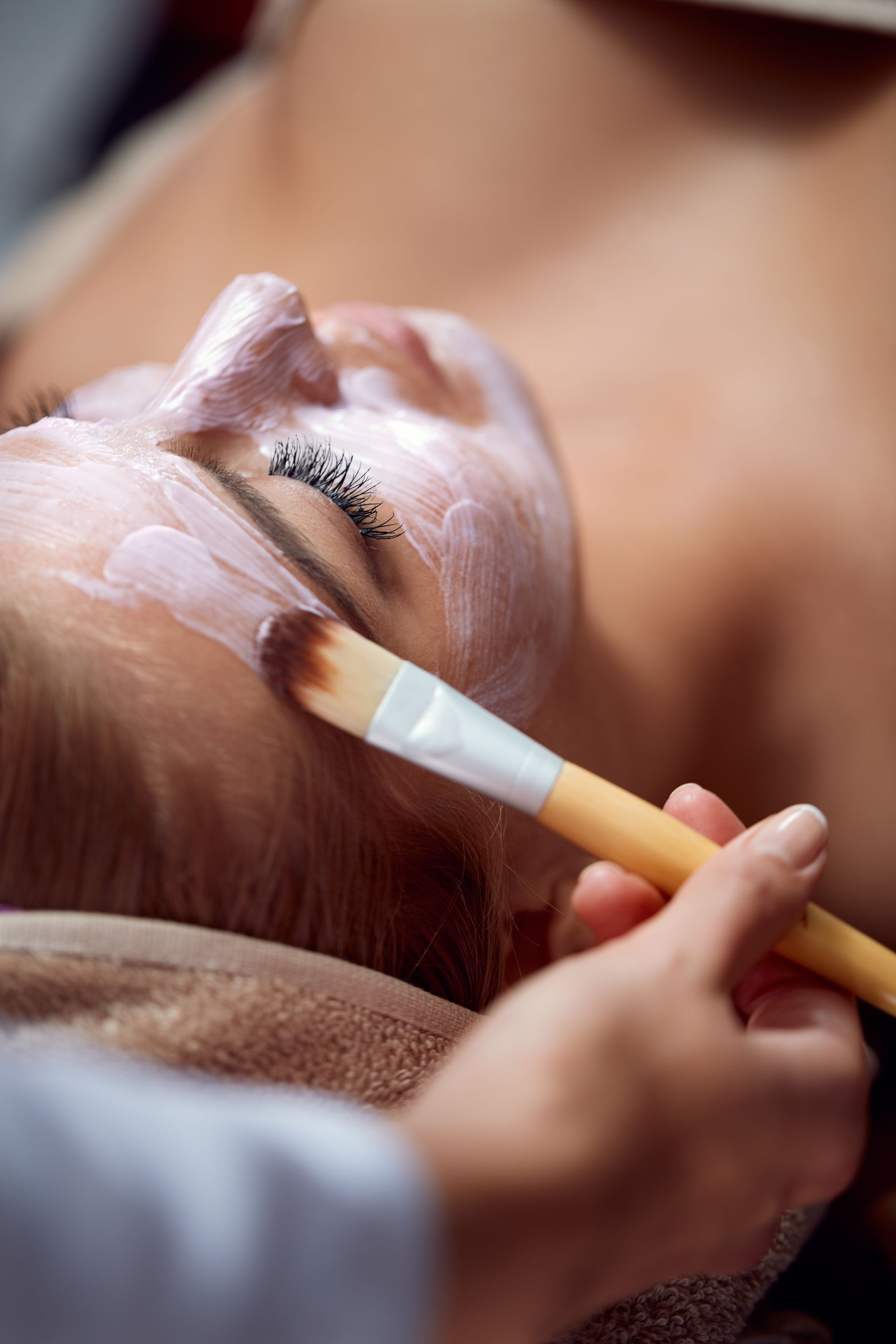 Une personne tenant un pinceau applique la crème sur le visage d'une femme