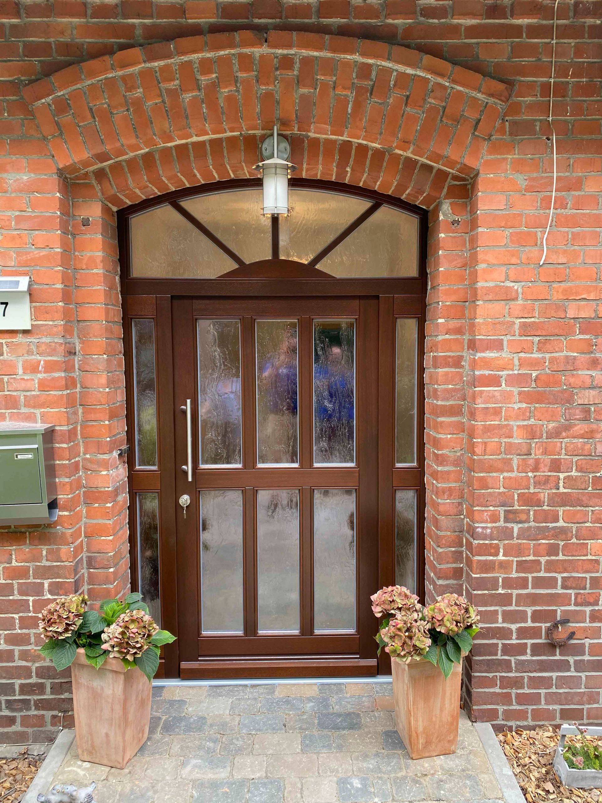 Ein Backsteingebäude mit einer Holztür und zwei Topfpflanzen davor