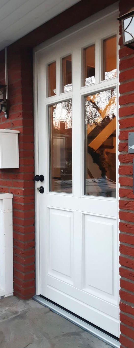 An einer Backsteinmauer neben einem Briefkasten steht eine weiße Tür.