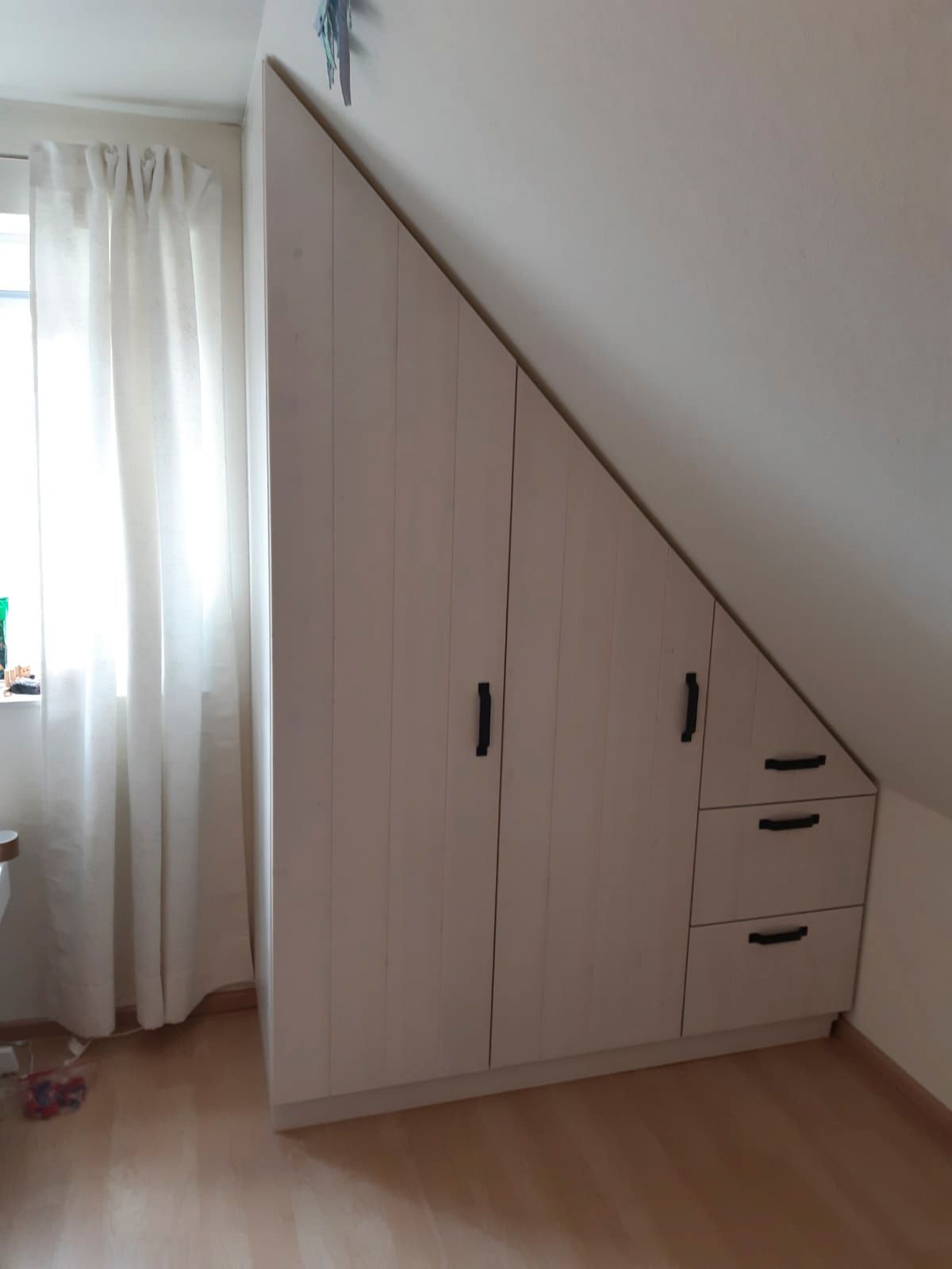 Ein Zimmer mit einem Schrank unter der Treppe und einem Fenster.