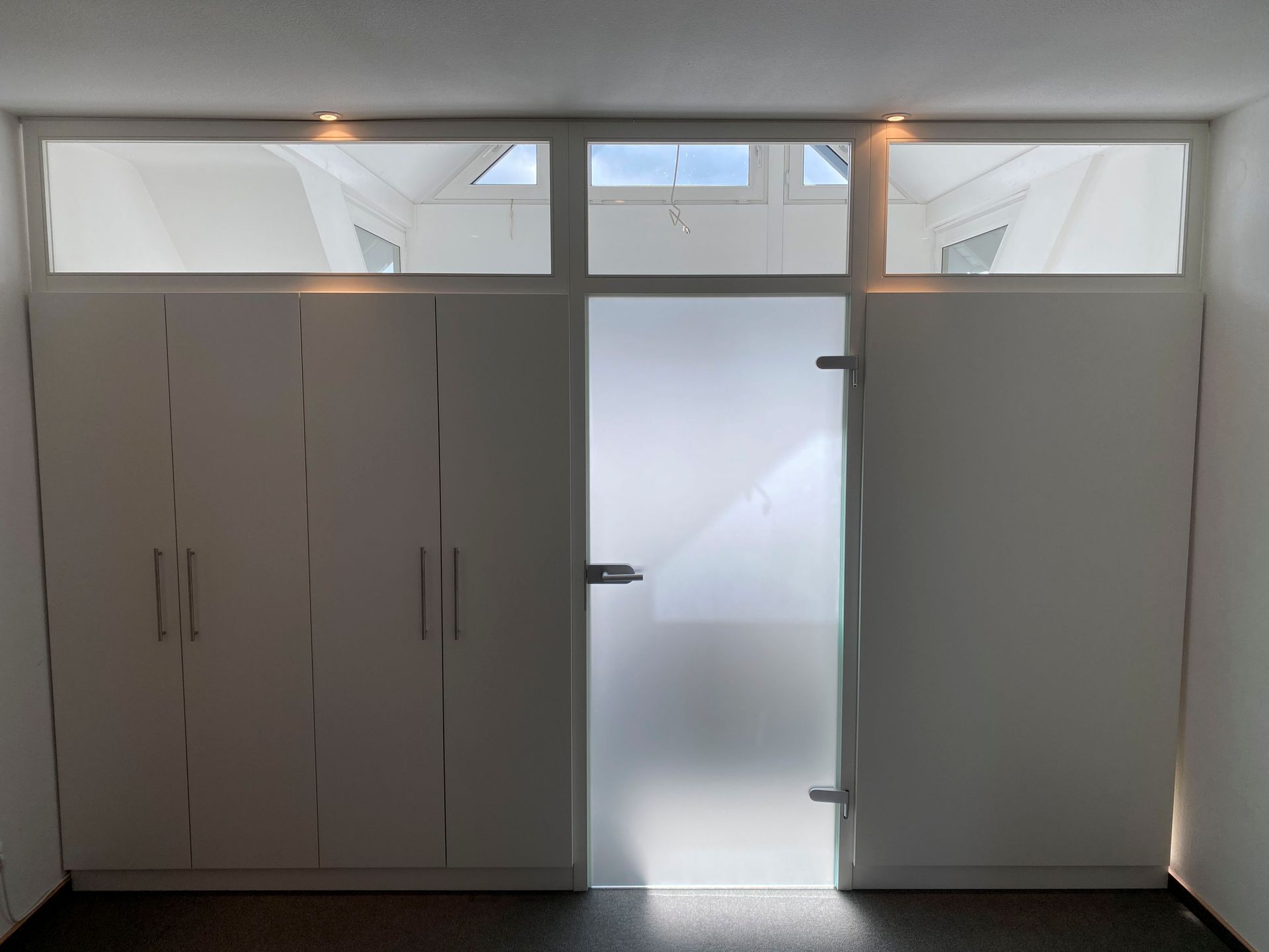 Ein Raum mit weißen Schränken und einer Milchglastür.