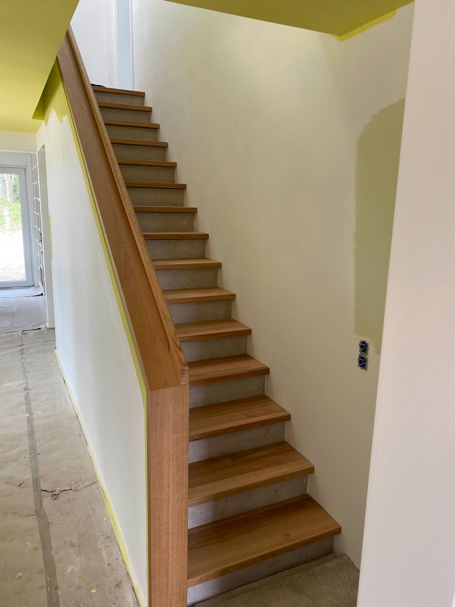 Eine Holztreppe führt eine weiße Wand in einem Flur hinauf.