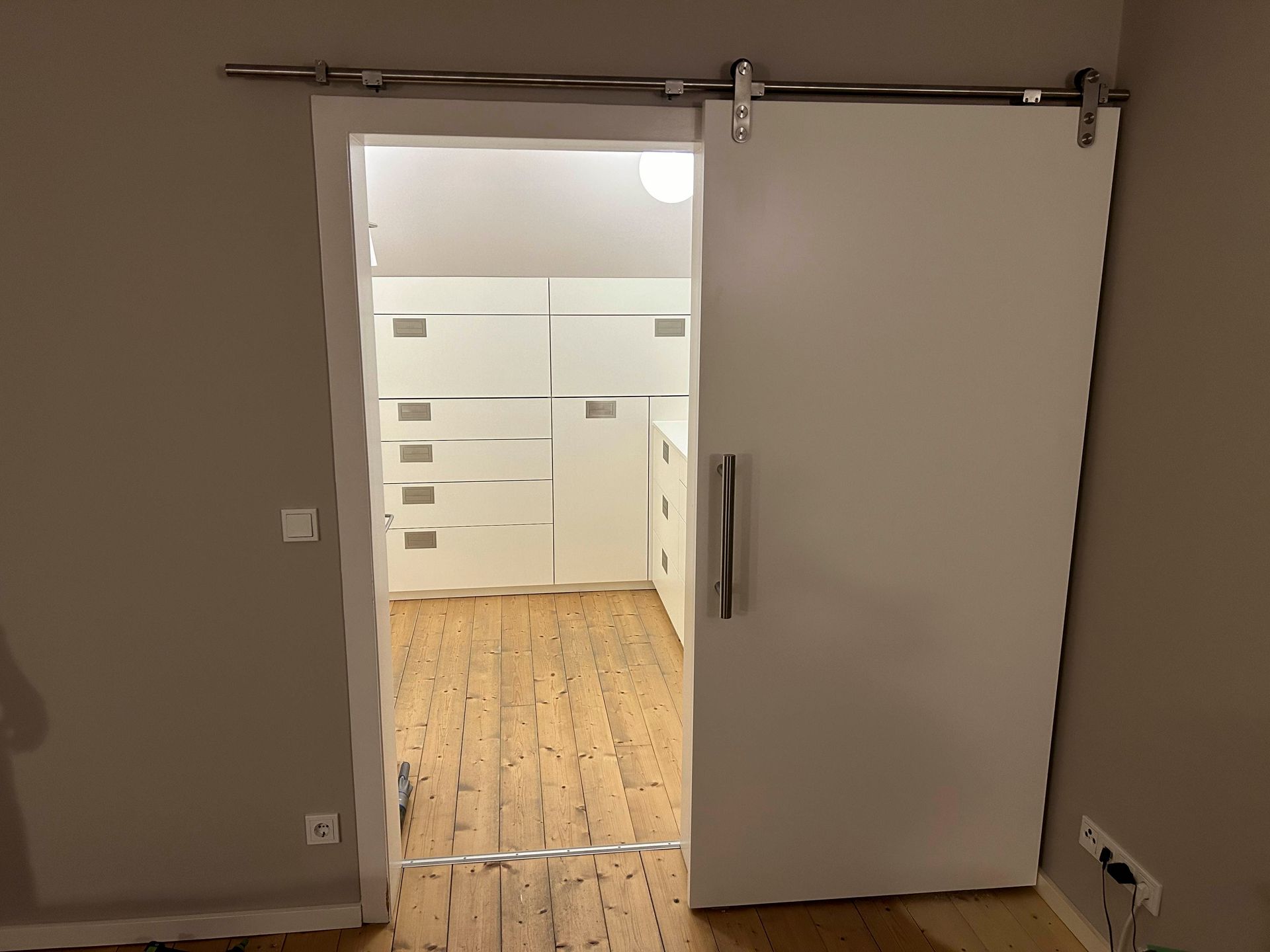 Durch eine Schiebetür gelangt man in einen Raum mit Holzboden.