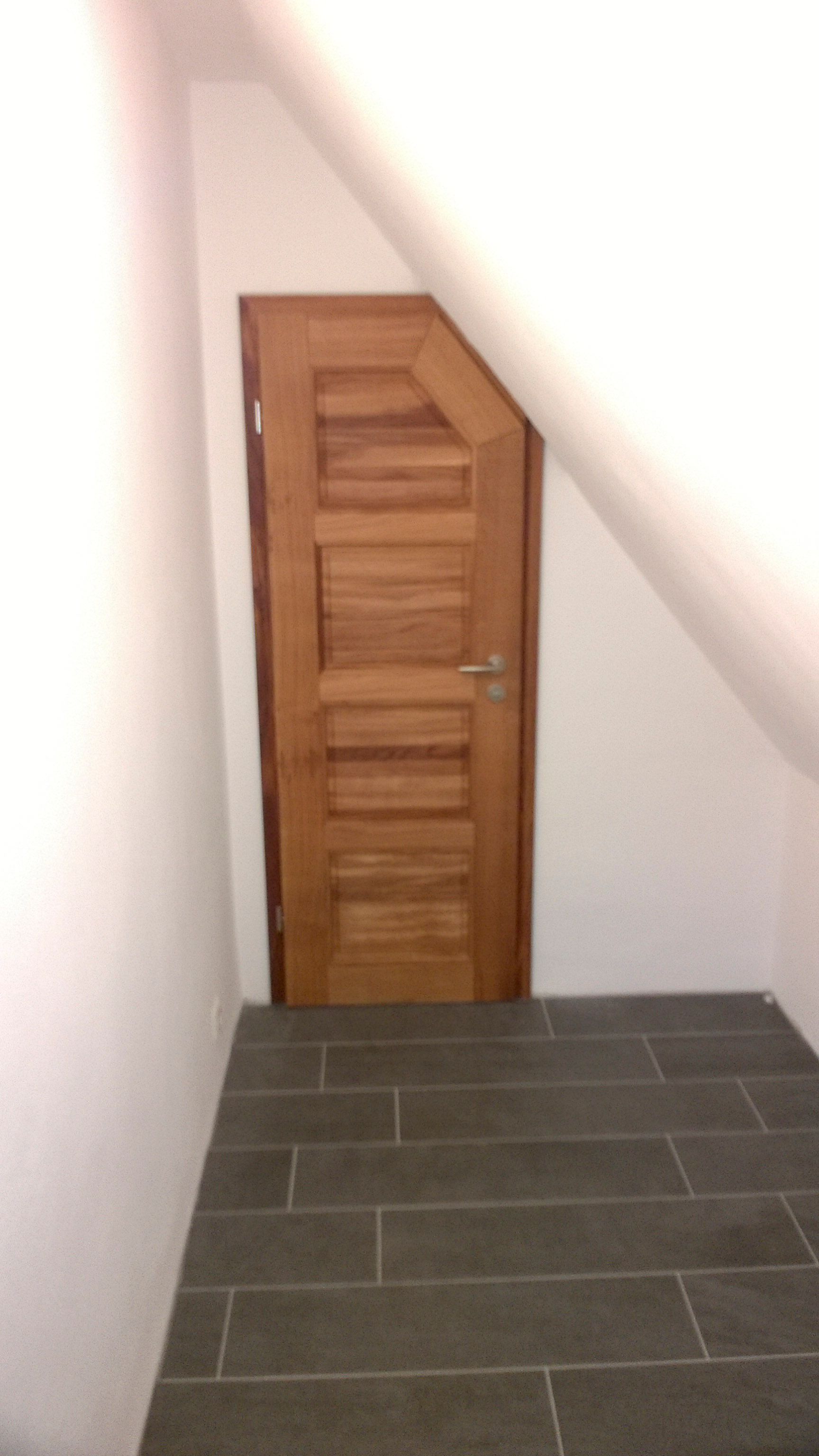 In der Ecke eines Flurs befindet sich eine Holztür.