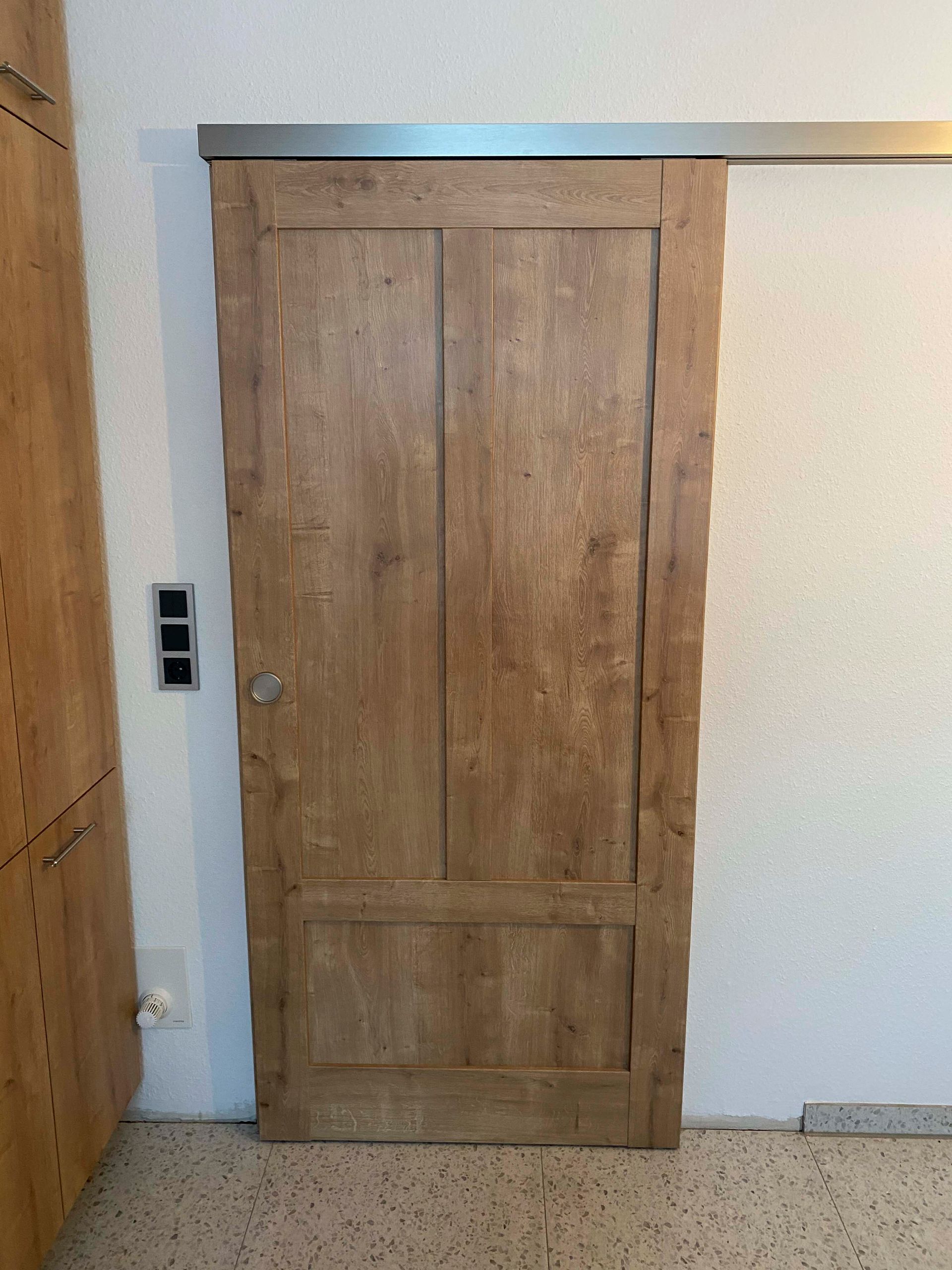 An einer weißen Wand in einem Raum hängt eine hölzerne Schiebetür.