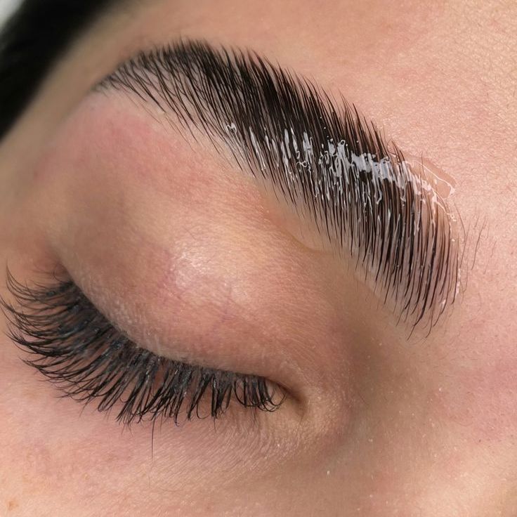 Un gros plan de l'œil d'une femme avec de longs cils et un sourcil brillant.