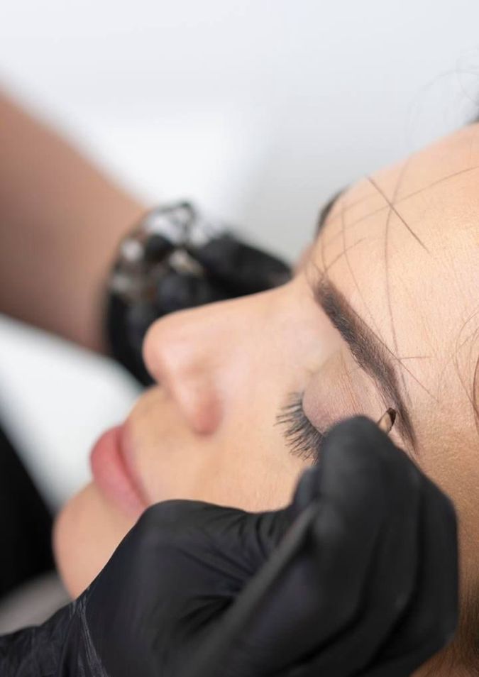 Une femme se fait épiler les sourcils par une personne portant des gants noirs.