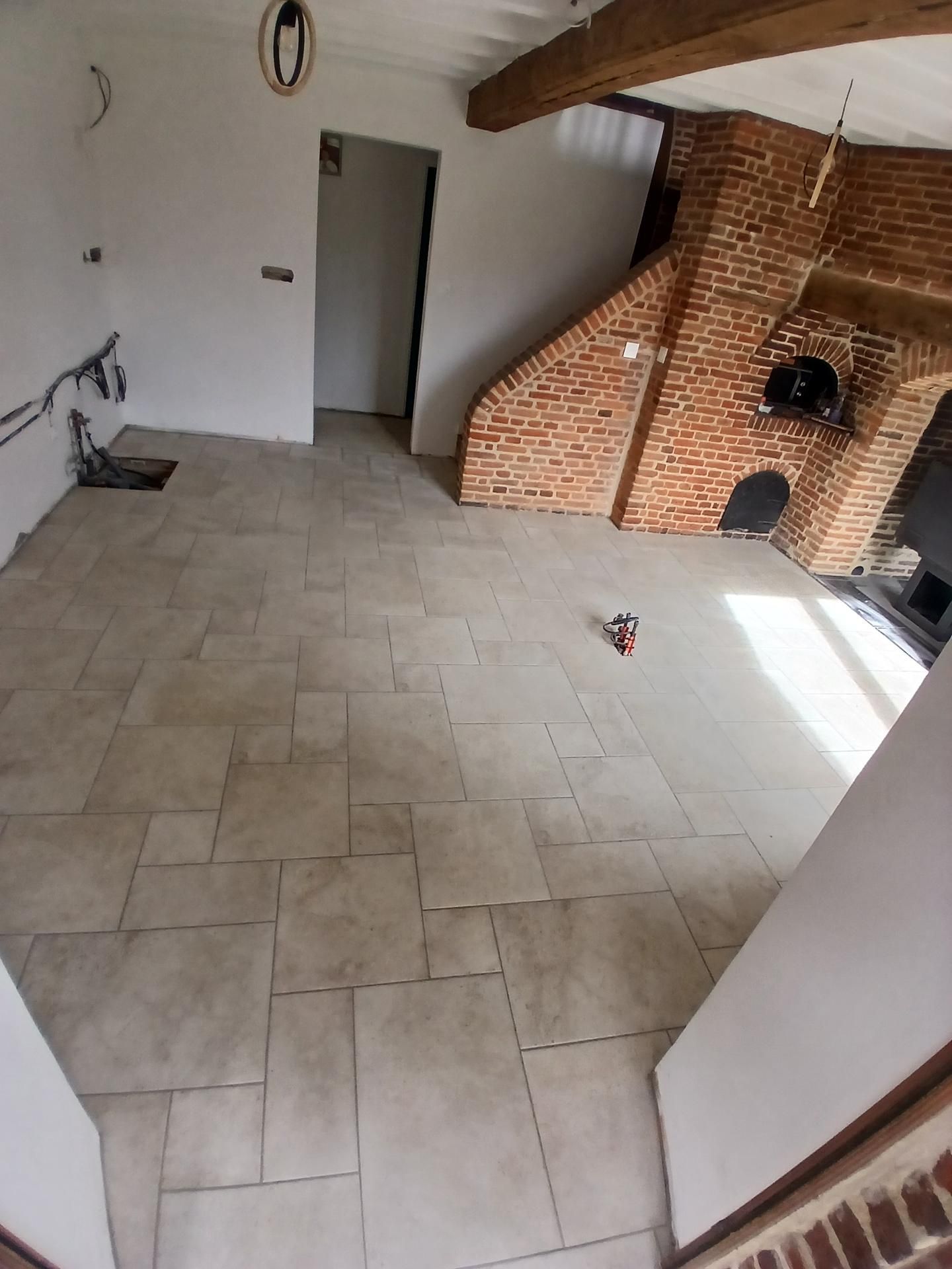 Pièce carrelée vide avec des murs blancs, une cheminée en briques et une porte ouverte.
