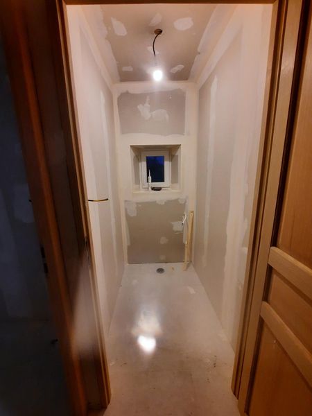 Cloisons, carrelage et petite fenêtre dans une pièce longiligne.