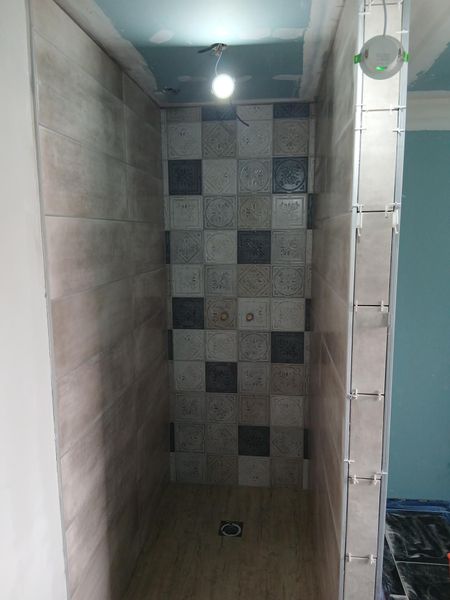 Pose de faïence dans une cabine de douche avec une ampoule pendant du plafond.