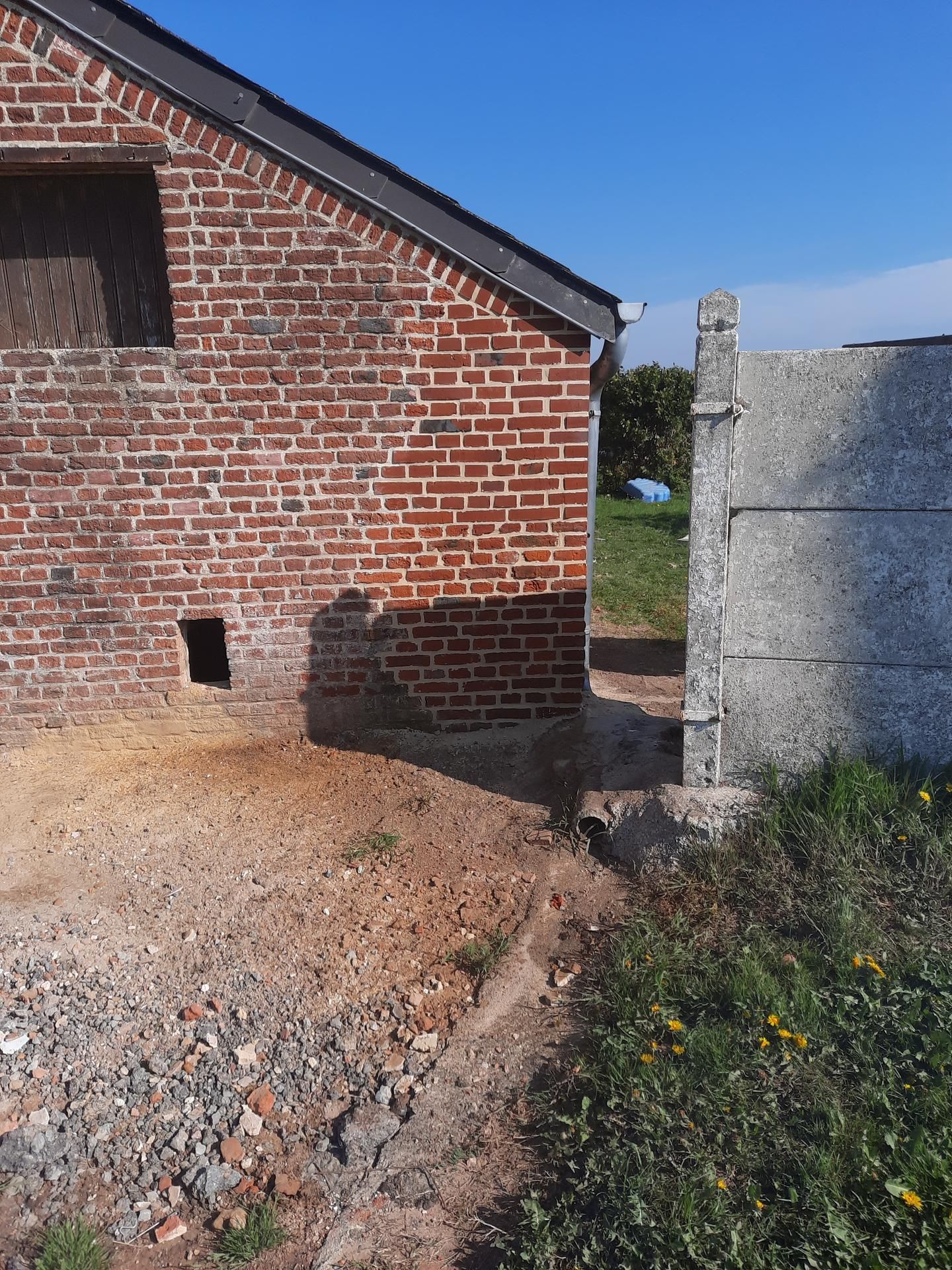 Bâtiment en briques à côté d'un chemin de gravier et d'un mur en béton sous un ciel bleu clair.