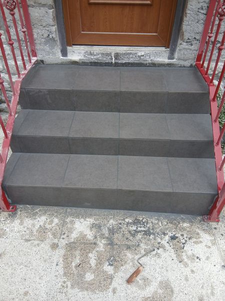 Escalier en carrelage avec des rambardes rouges devant une porte.