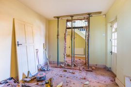 Pièce partiellement démolie avec des débris, des montants apparents et un mur vitré lors de travaux de rénovation.