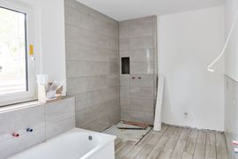 Salle de bains en cours de rénovation avec des murs carrelés en béton brut, une baignoire, une fenêtre et un coin douche.