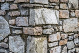 Gros plan sur un mur de pierres empilées, composé de roches irrégulières grises et beiges.
