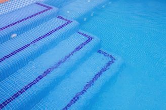 Una piscina con azulejos azules y rayas moradas en los escalones.