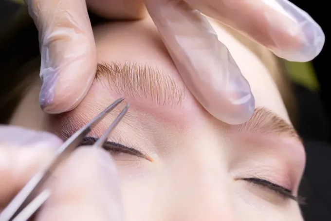 Primer plano de la depilación de la ceja de una persona. La persona tiene los ojos cerrados, maquillaje.