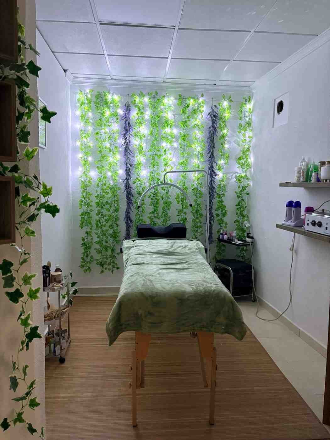 Sala de spa con mesa de masajes, enredaderas verdes y luces.