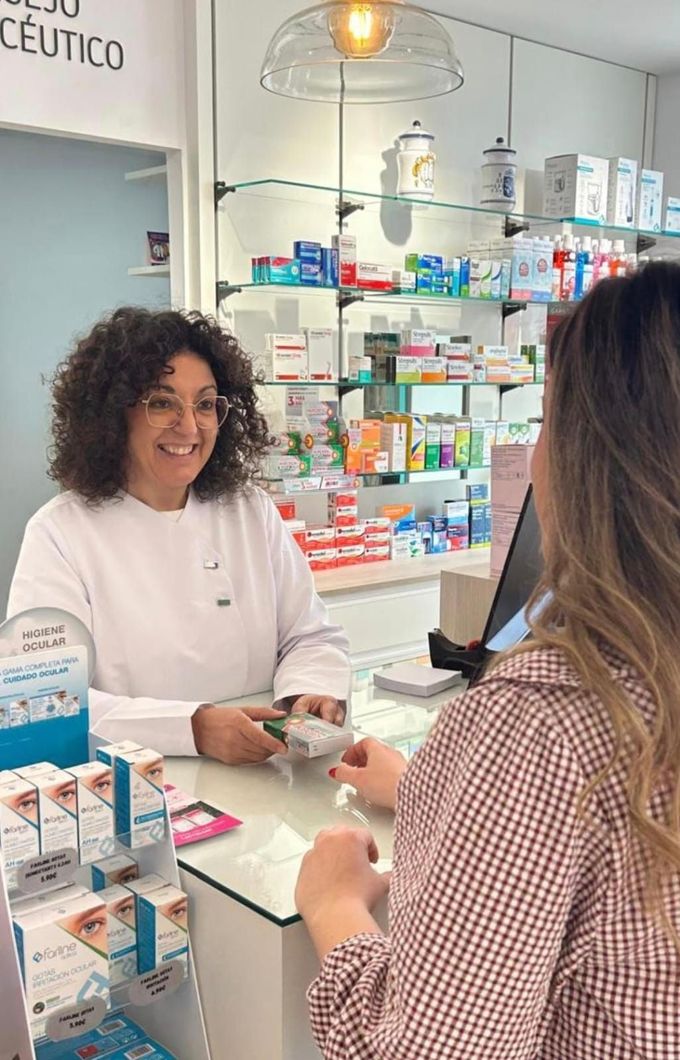 Farmacéutico mostrando medicamentos a una mujer y un niño en una farmacia; sonriendo.