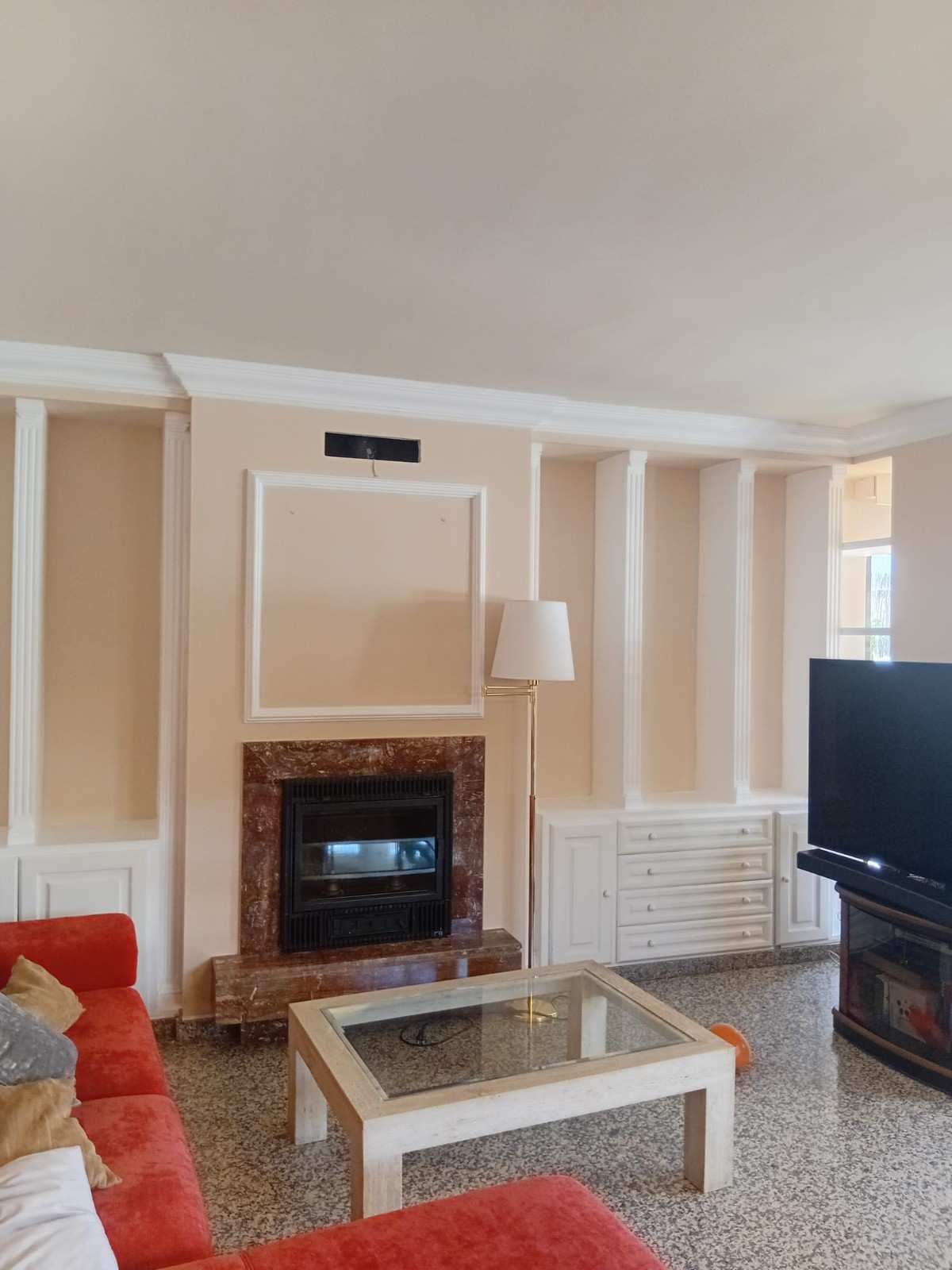 Sala de estar con chimenea, mesa de centro de cristal, sofá rojo, lámpara de pie y televisor a la derecha.