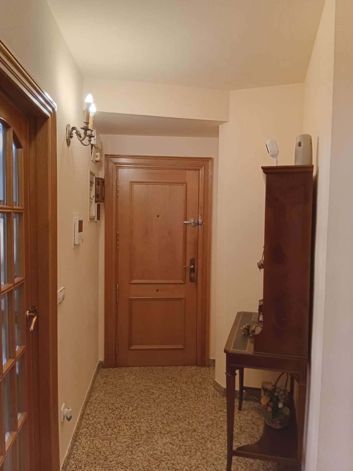 Pasillo estrecho con puertas de madera, apliques de pared y un pequeño banco debajo de un armario.