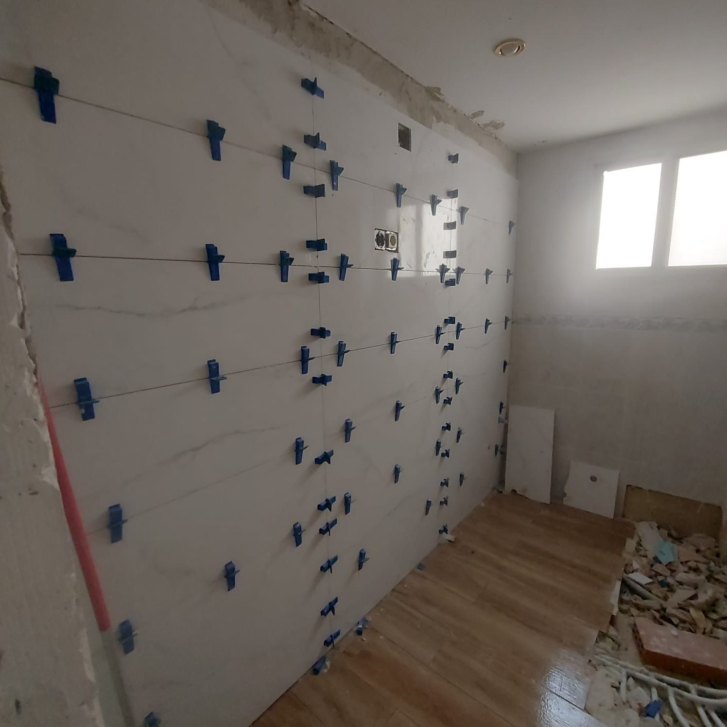 Un pintor aplica pintura blanca en la esquina de una pared con un rodillo, subido a una escalera.