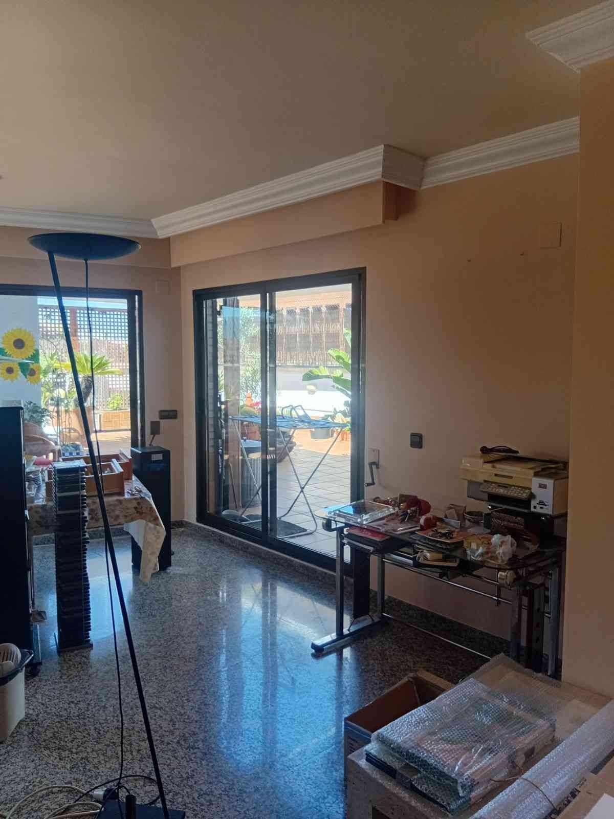 Sala de estar luminosa con puertas de cristal, muebles dispersos y una mesa con artículos del hogar.