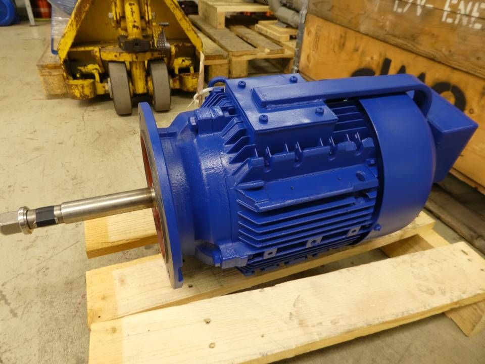 Blauer Industrie-Elektromotor auf einer Holzpalette in einer Werkstatt, aus dem eine Metallwelle herausragt.