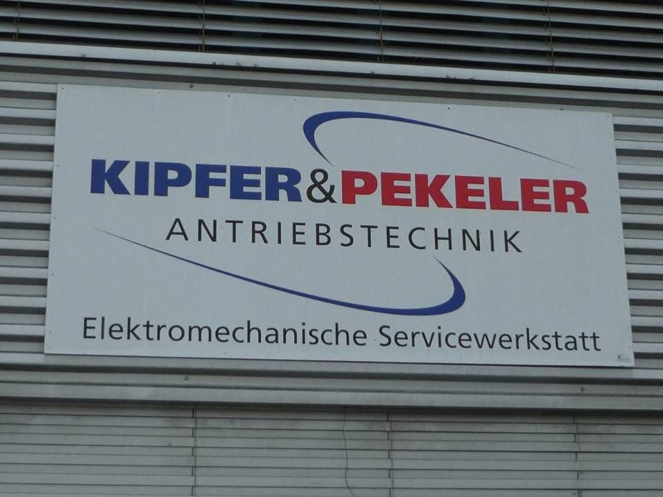 Zwei Personen in blau-schwarzen Overalls stehen neben einer grossen Maschine in einer Werkstatt.