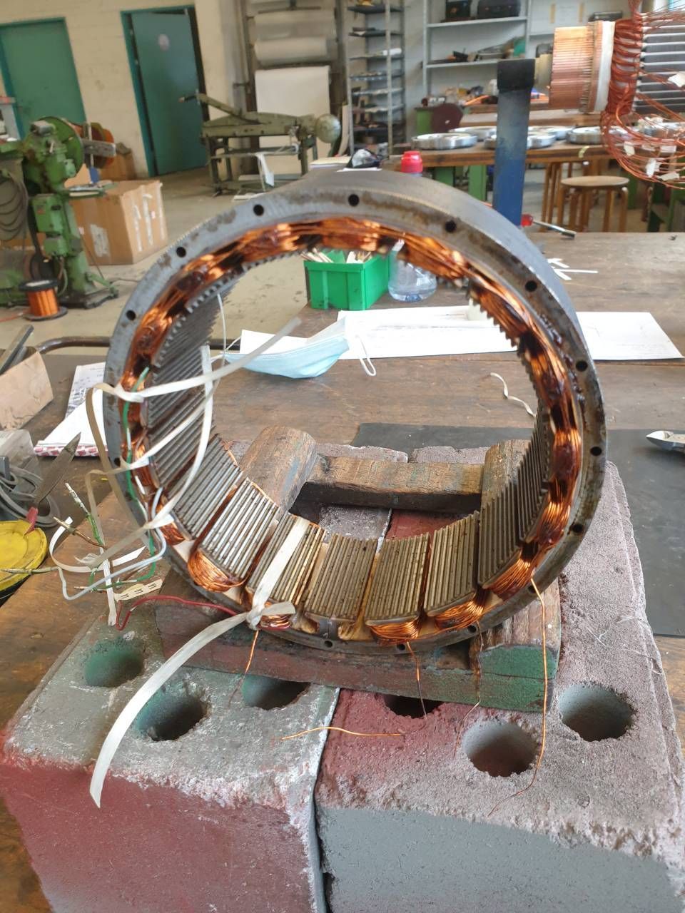 Beschädigte Statorspule eines Elektromotors liegt in einer Werkstatt auf Betonblöcken.