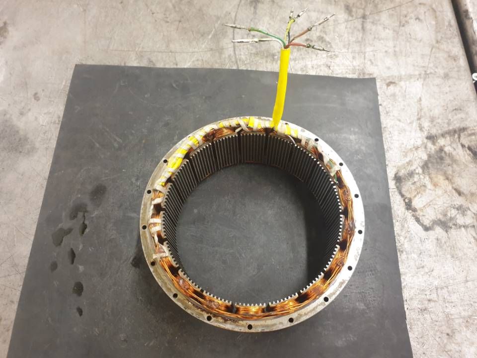 Runder Stator eines Elektromotors mit gelben Drähten auf einer dunklen Werkbank