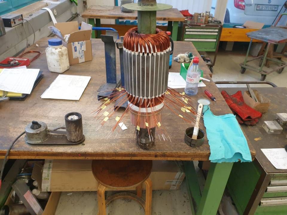 Werkstatttisch mit einem in der Mitte befindlichen, kupfergewickelten Elektromotor oder Generator.