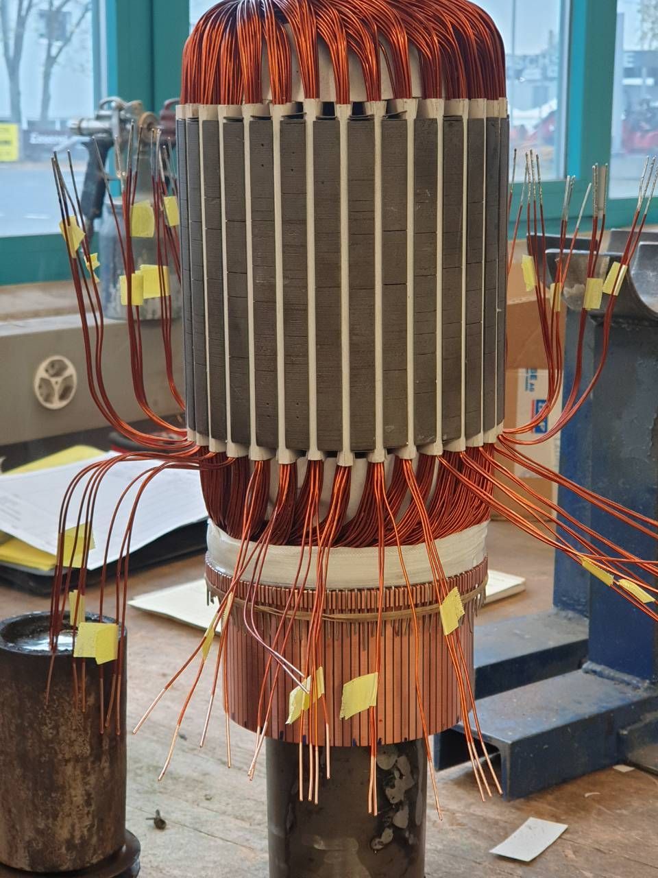Grosser Elektromotor- oder Transformatorkern mit Kupferwicklungen in einer Werkstatt, umgeben von Drähten auf einem Ständer