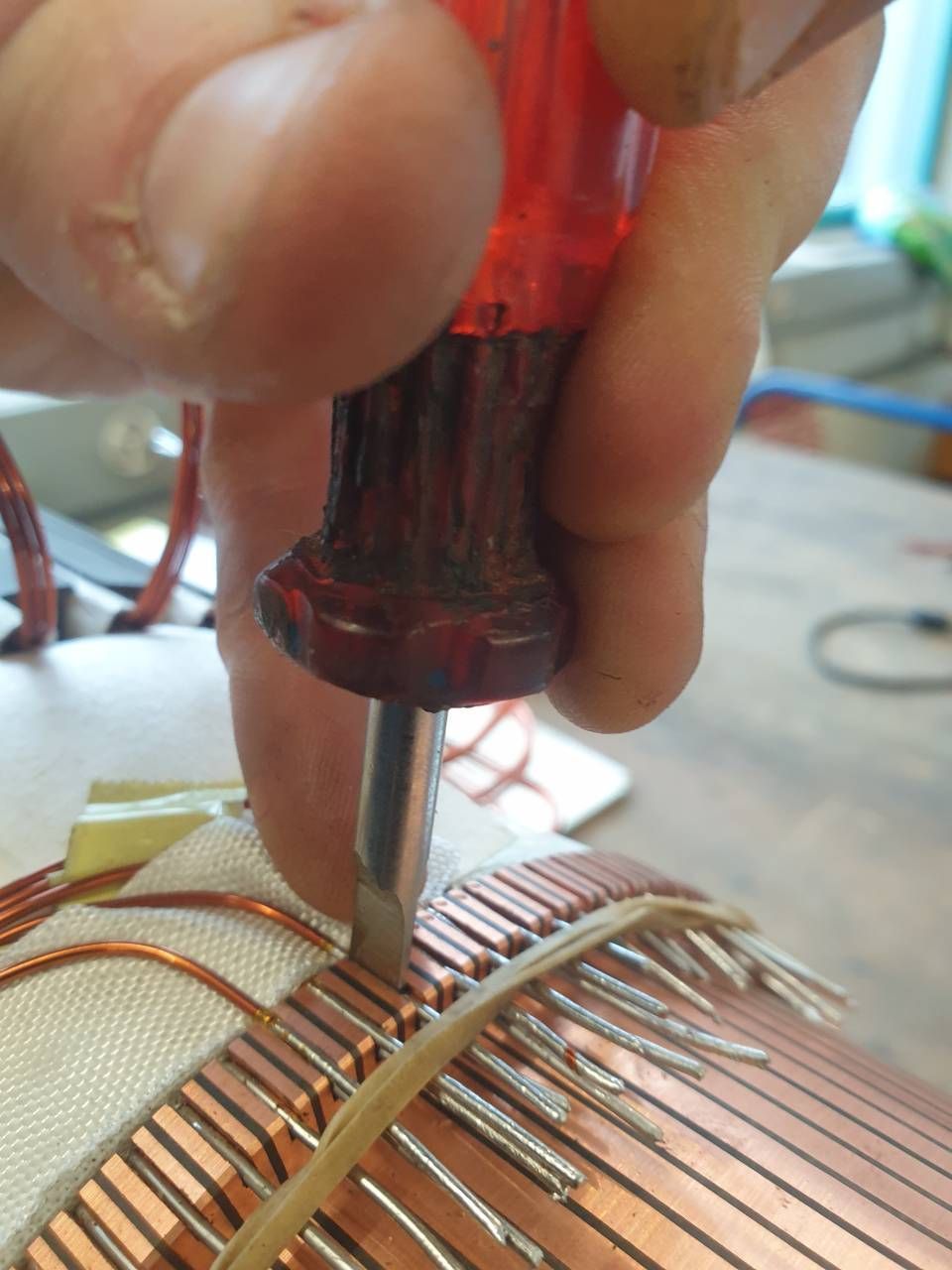 Hand benutzt einen Schraubendreher, um dünne Metalldrähte an einer kleinen elektronischen Spulenbaugruppe einzustellen
