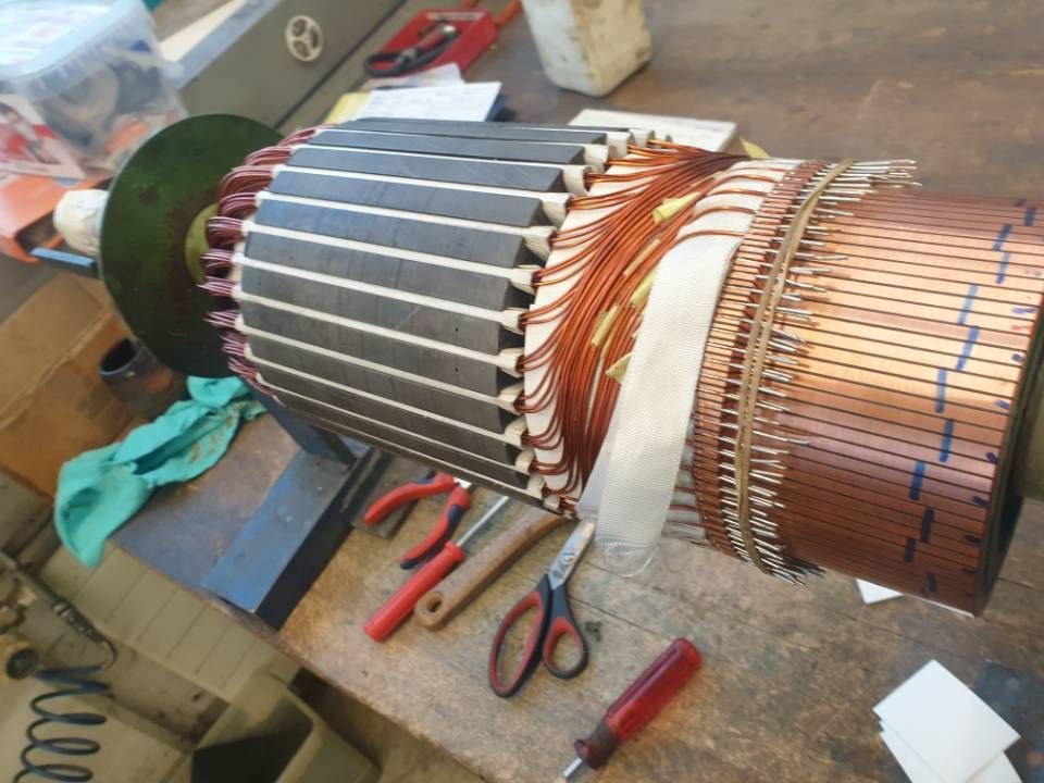 Der auf einer Werkbank zerlegte Motor zeigt Kupferwicklungen, Metallbleche und in der Nähe liegende Handwerkzeuge.