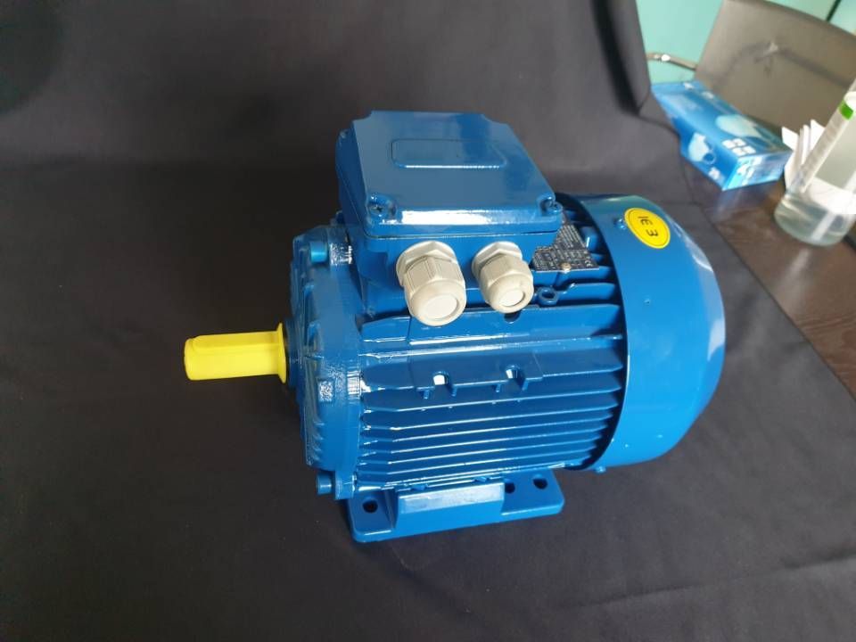 Blauer Elektromotor mit gelber Welle auf dunklem Untergrund.