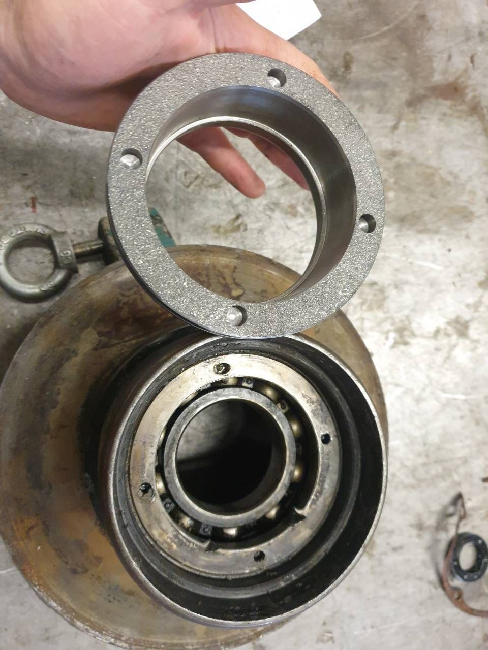 Hand, die einen Metallring über einer kreisförmigen mechanischen Lageranordnung auf einer Werkbank hält