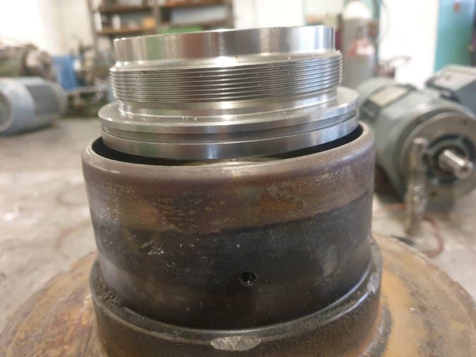 Nahaufnahme eines industriellen Metallbauteils mit Gewindekopf und verrostetem Sockel in einer Werkstatt
