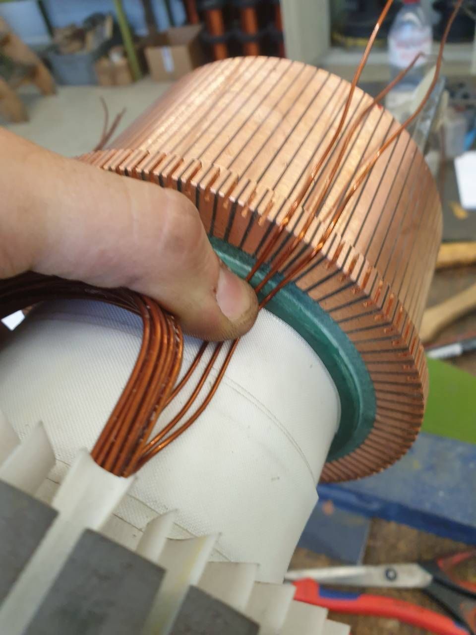 Kupferdraht wird von Hand um einen weissen zylindrischen Motorkern gewickelt, wobei die Spule mit einer Hand gehalten wird.