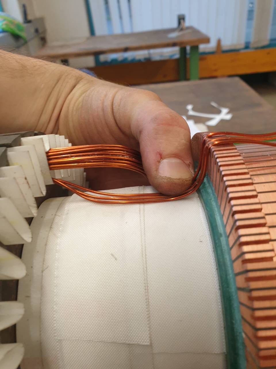 Handwicklung von Kupferdraht um einen weissen Spulenkern eines Elektromotors