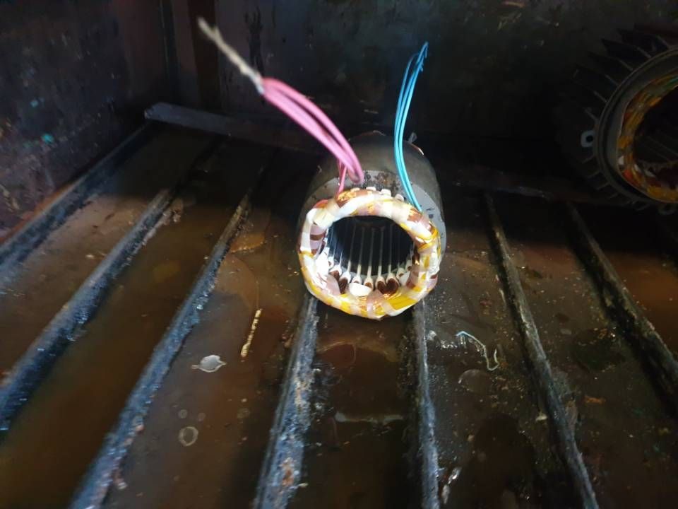Ein durchgebrannter Stator eines Elektromotors mit freiliegenden farbigen Drähten in einer dunklen Industrieumgebung
