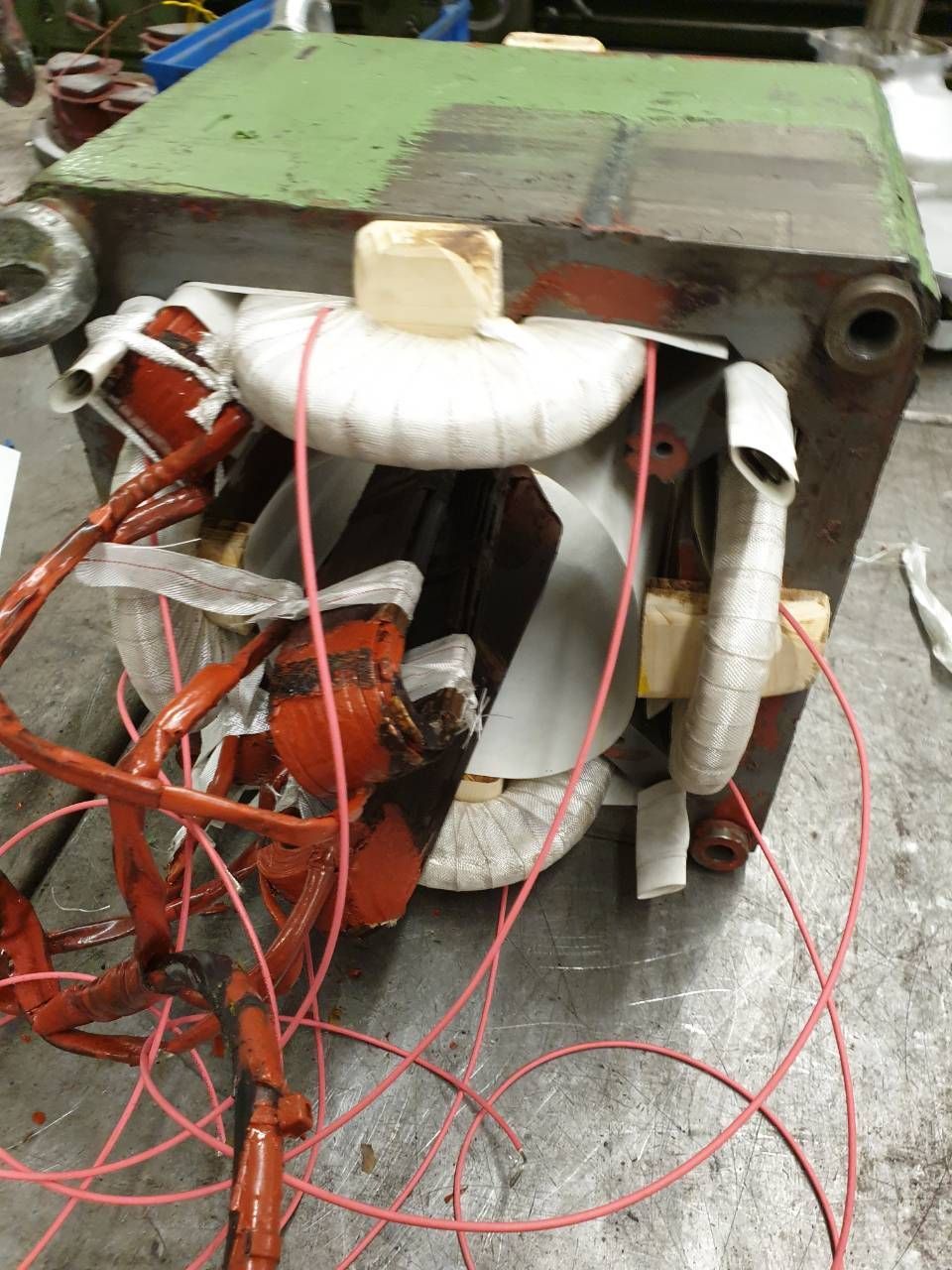 Beschädigtes elektrisches Gerät mit freiliegenden roten Drähten und weissen Spulen auf einer Werkbank.