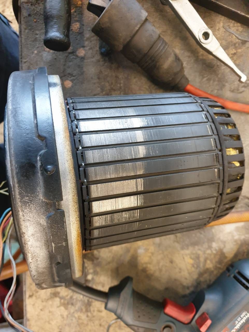 Zylindrischer Motorrotor mit Kupfersegmenten auf einer Werkbank, umgeben von Werkzeugen.
