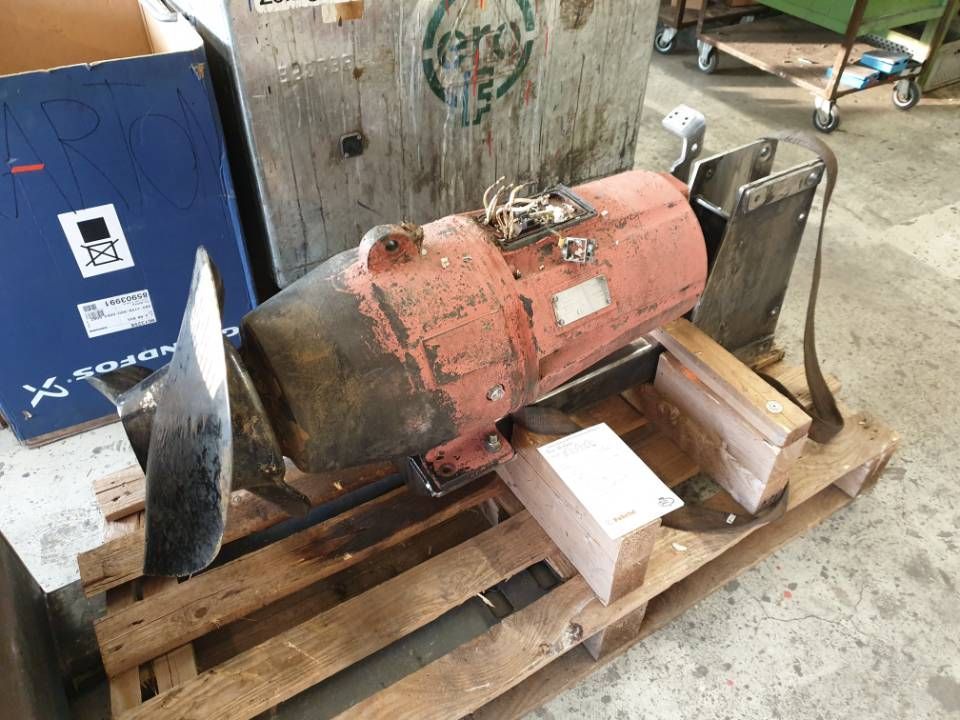 Ein verrosteter Industriemotor auf einer Holzpalette in einer Werkstatt, daneben liegen Metallteile.