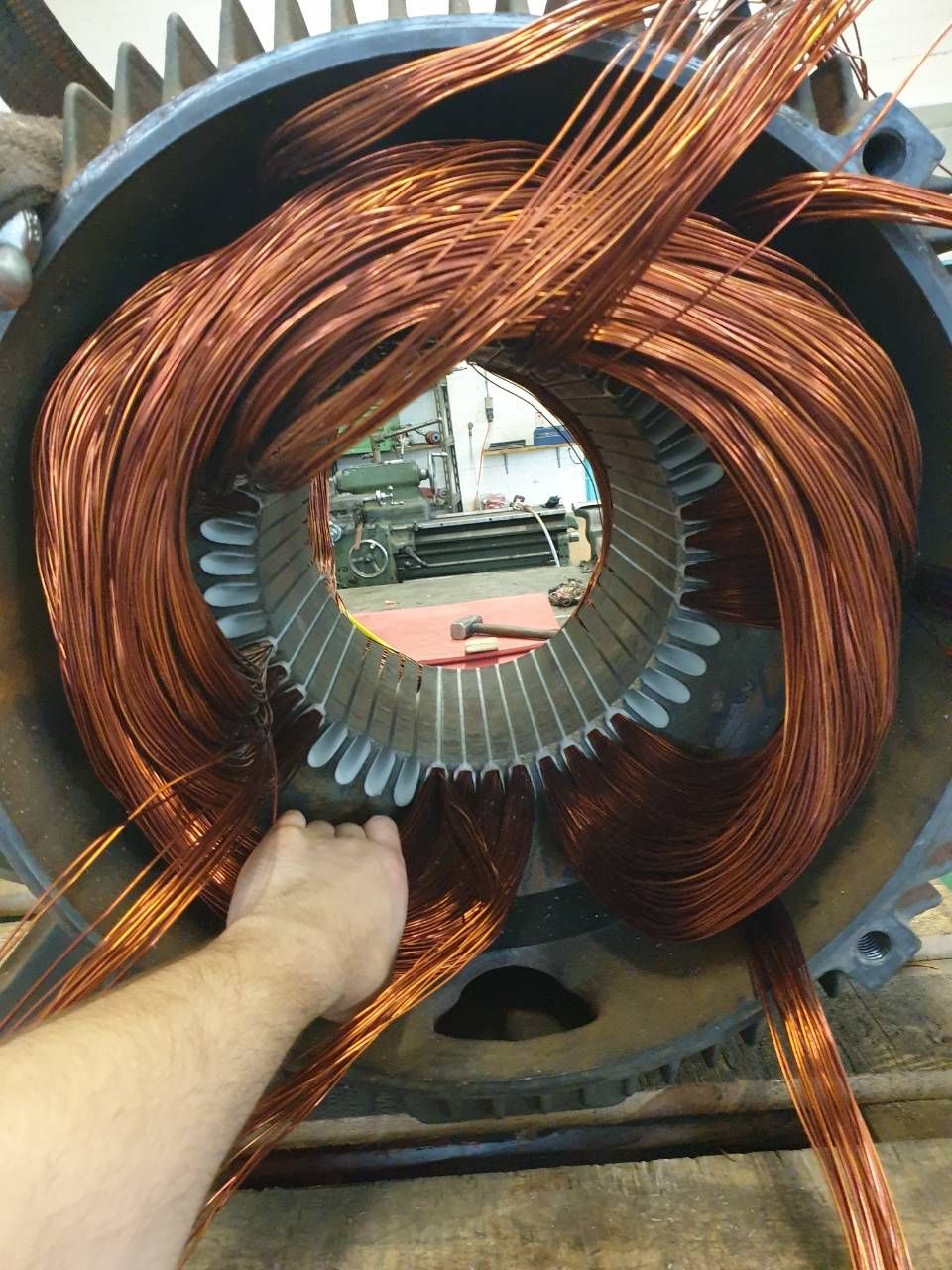 Kupferwicklungen werden im Stator eines grossen Elektromotors installiert, wobei eine Hand die Spule hält.