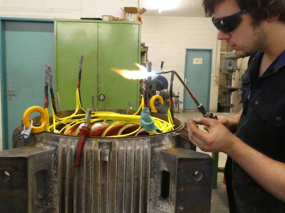 Ein Techniker arbeitet mit einem Schweissbrenner an farbigen Kabeln auf einer grossen industriellen Metallmaschine.