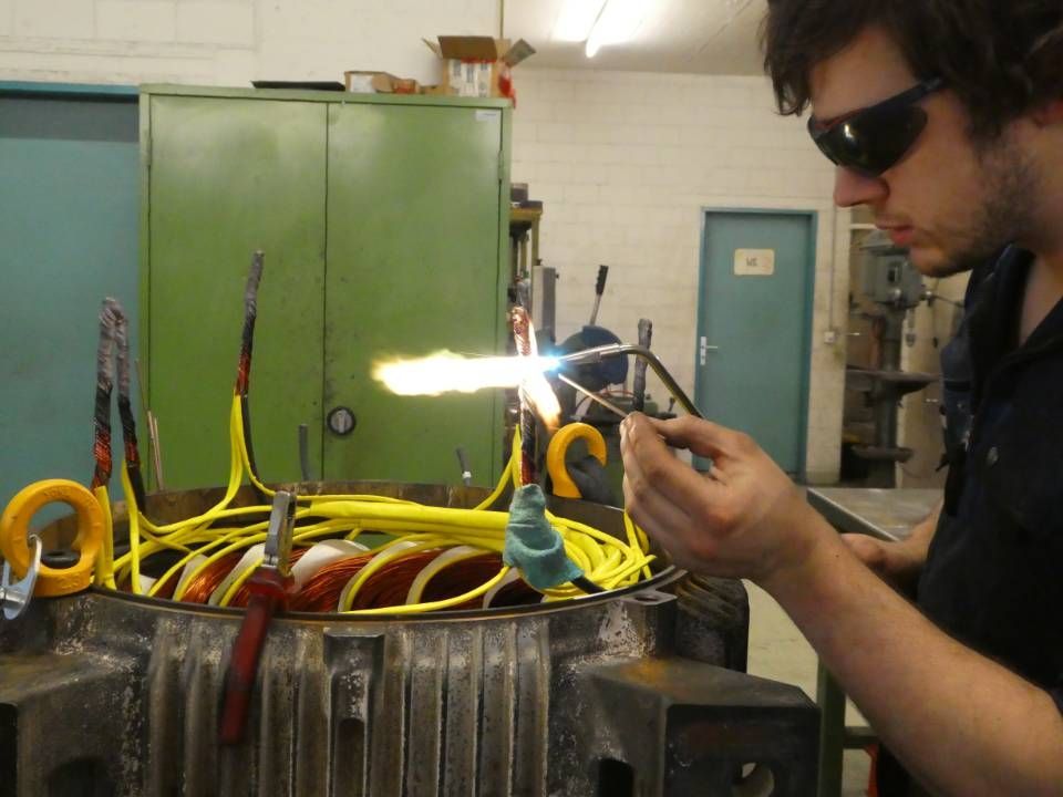 Eine Person schweisst in einem Metallbehälter, Funken sprühen in einer Industriehalle.
