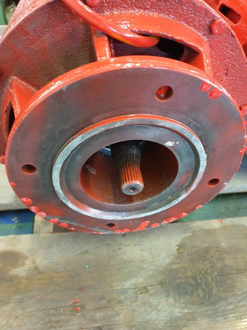 Nahaufnahme eines roten Industriemaschinengehäuses mit einer zentralen Metallwelle auf einem Betonboden