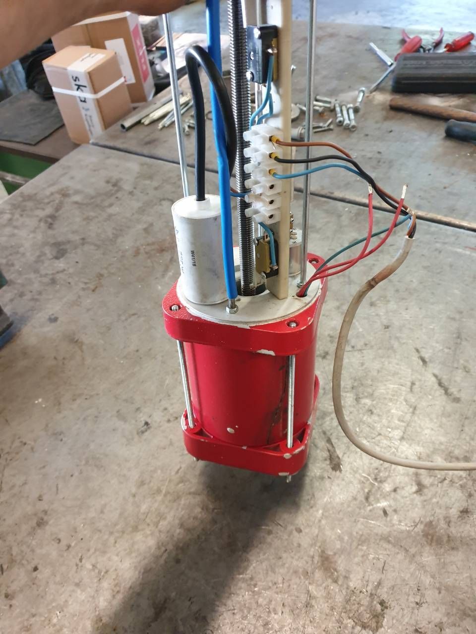 Eine rote Industriemaschine steht auf einem Betonboden in einer Werkstatt; oben sind Drähte und Schläuche angebracht.