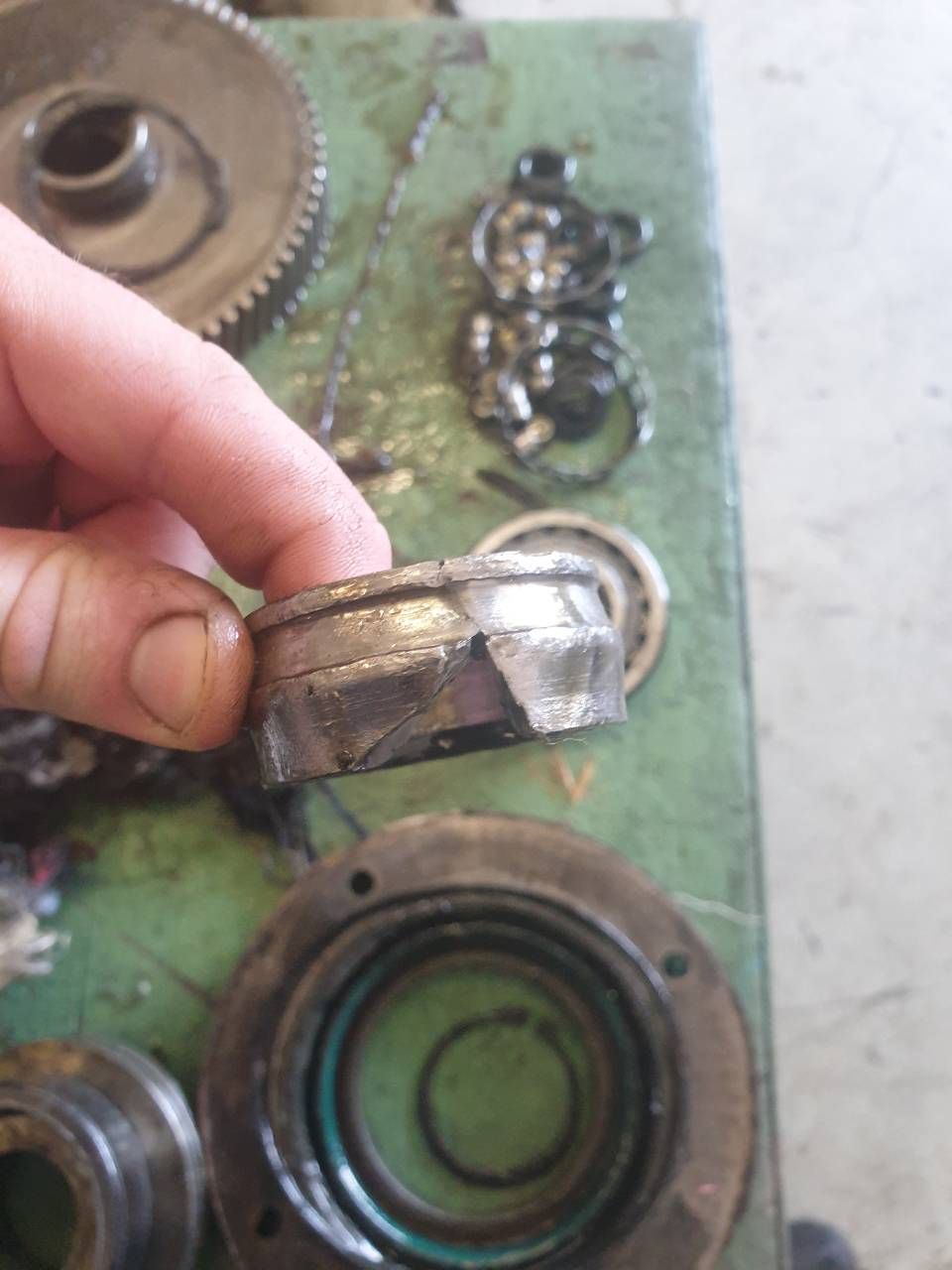 Eine Hand hält ein kleines Metalllager über ein grünes Maschinenteil mit kreisförmigen Komponenten.